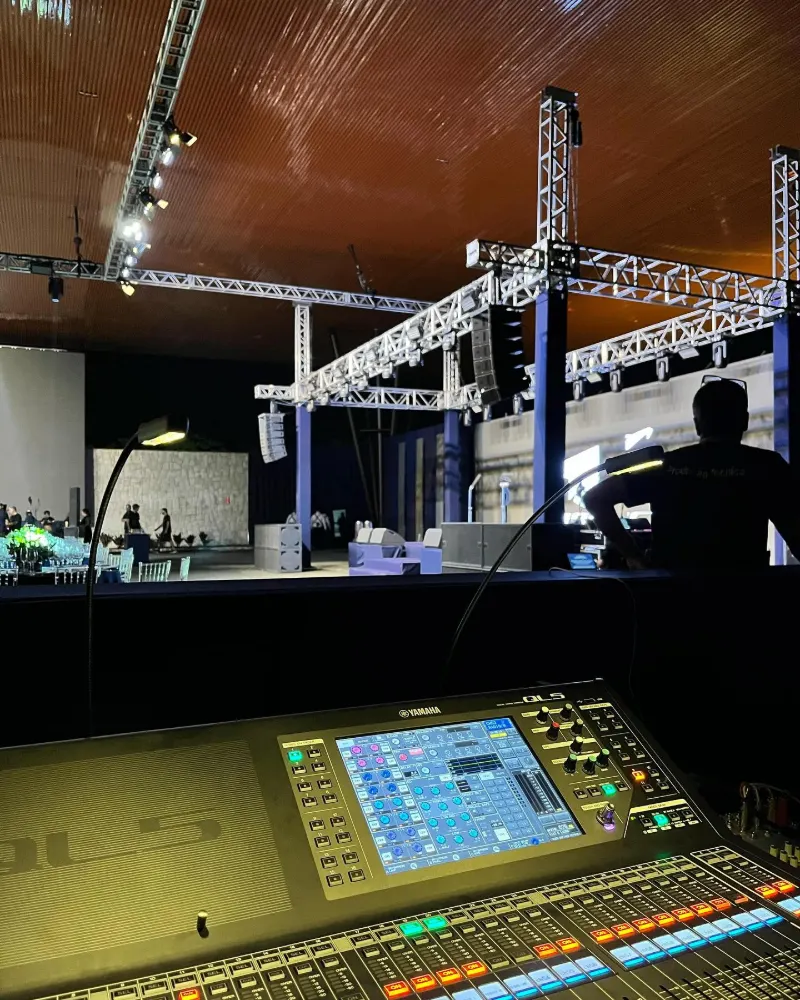 Mesa de som digital na técnica de um evento corporativo, com o palco e a treliça ao fundo