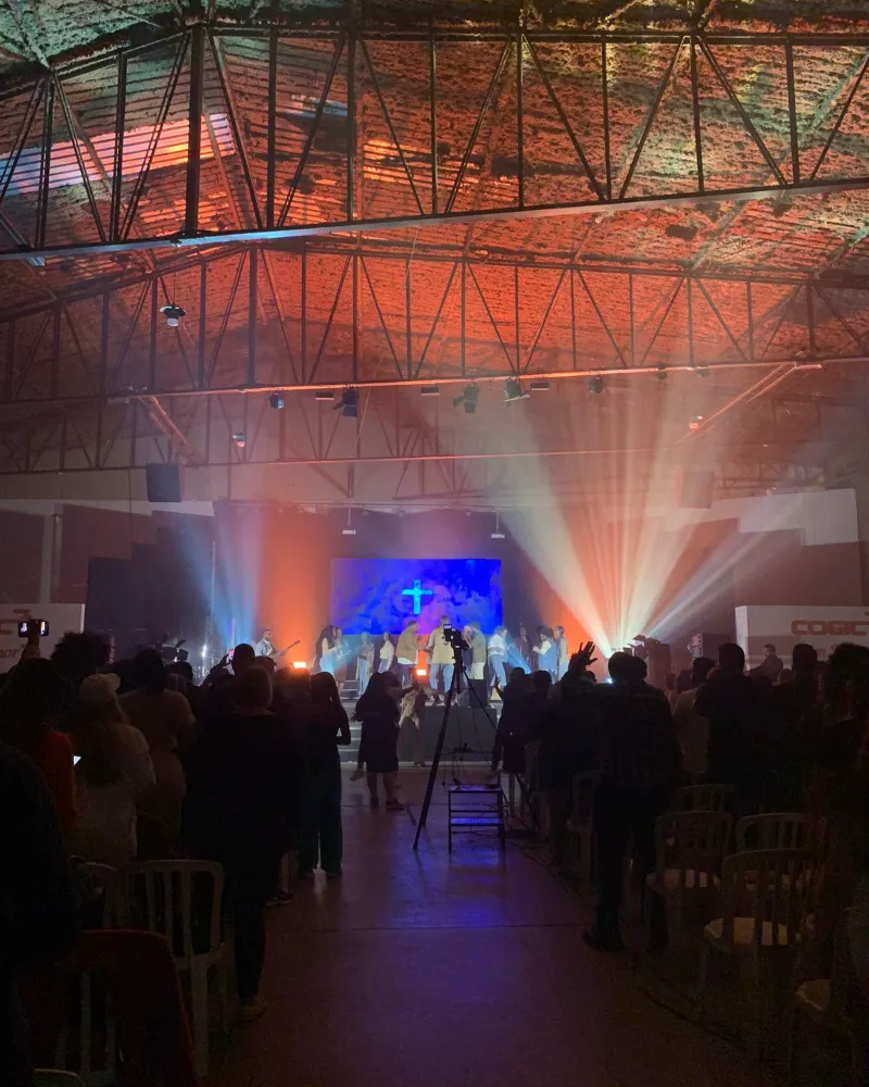 Feixes de luz coloridos sobre o palco e o público num galpão de eventos
