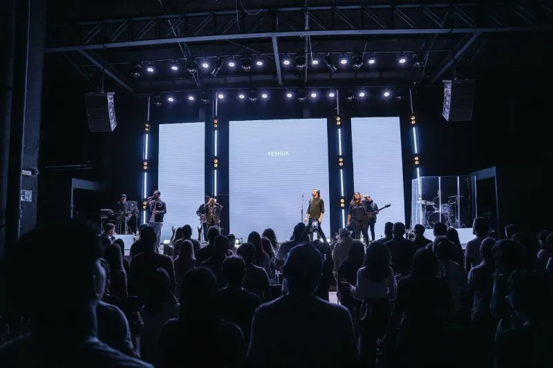 Palco com painel de LED ao fundo, luzes no teto e o público à frente
