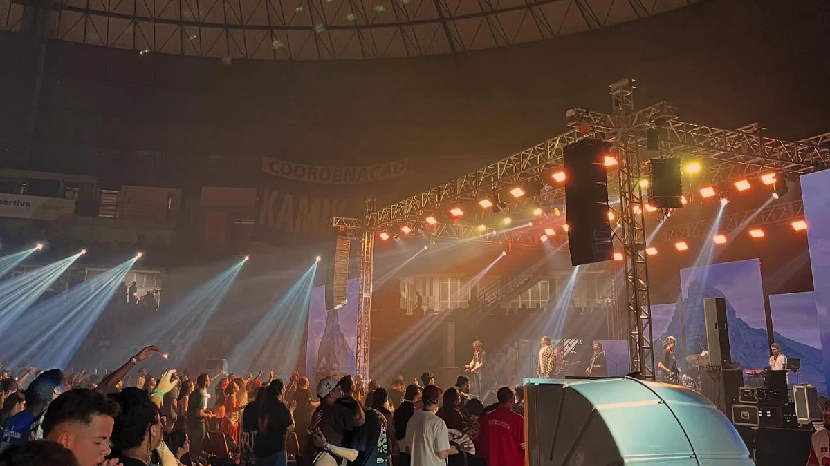 Show em arena lotada com line array pendurado na treliça e feixes de luz sobre o palco