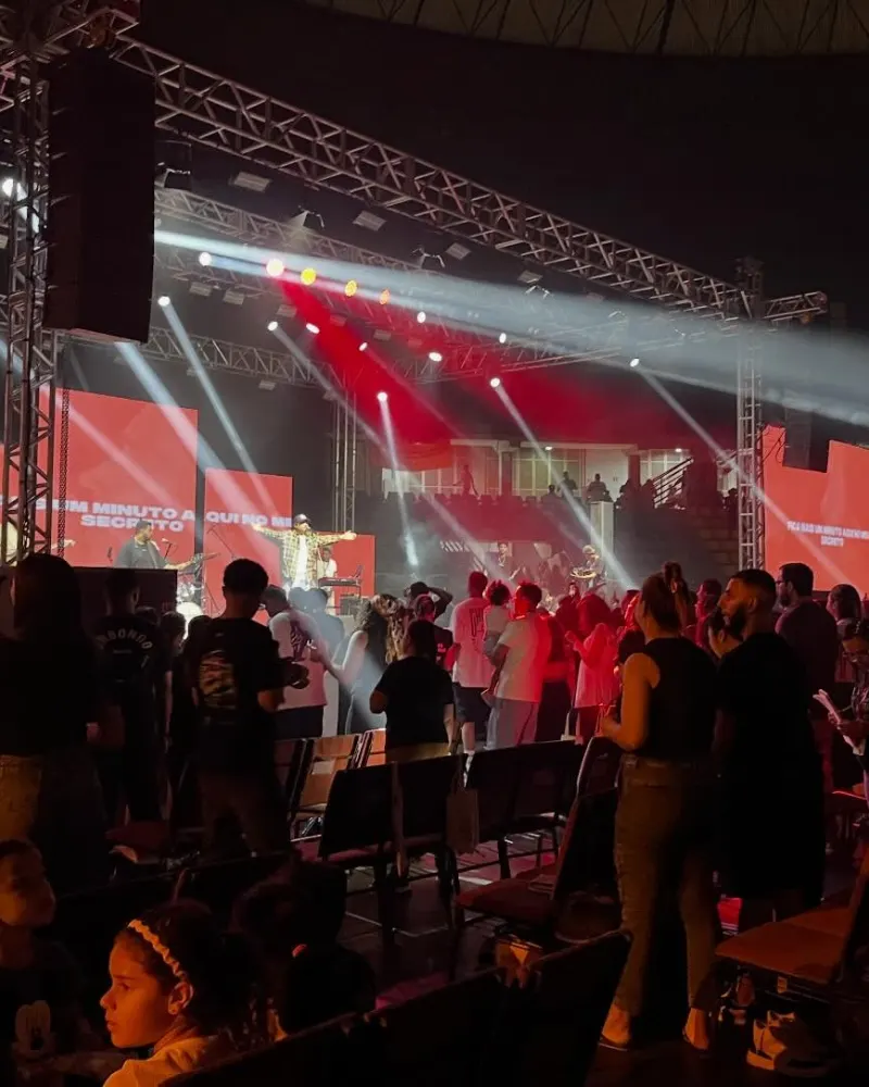 Show com luz vermelha no palco e caixa de som pendurada na treliça